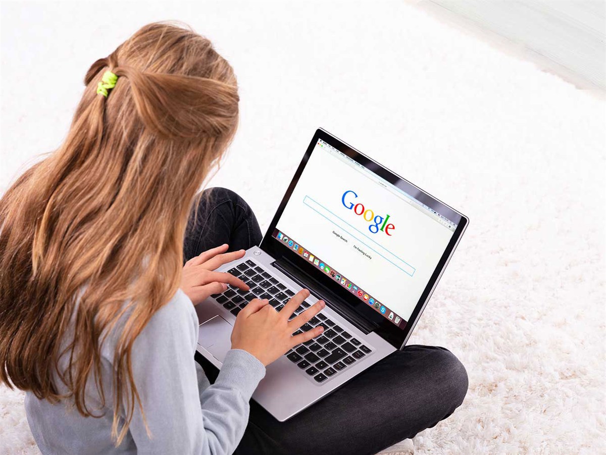 Frau sitzt mit dem Laptop auf dem Boden und sucht bei Google