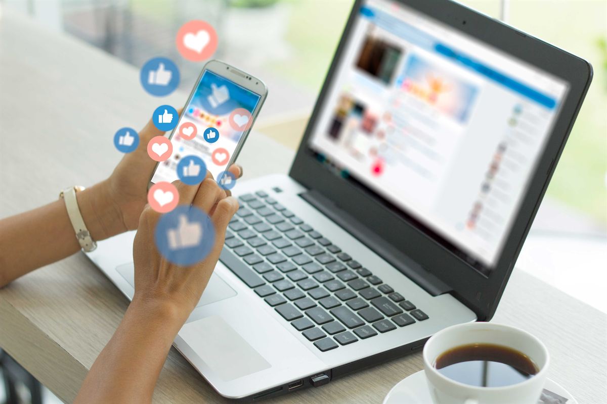 Smartphone mit Likes und Herzen vor einem Laptop mit sozialem Netzwerk
