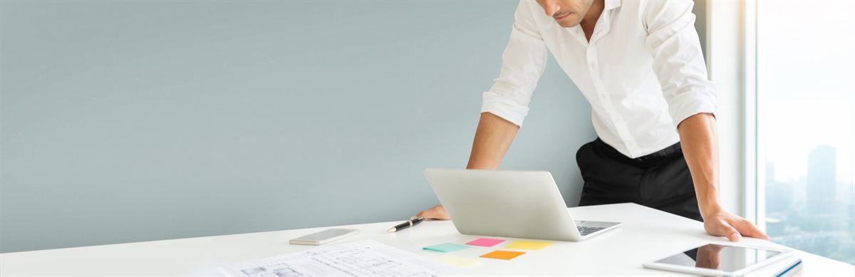 Webdesigner beugt sich in einem hellen Büro über einen Schreibtisch mit Laptop und Tablet